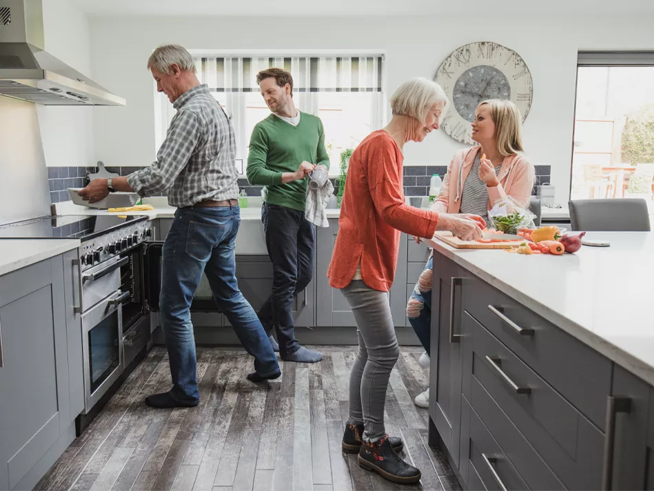 An elderly white couple and their adult son and daughter make a meal together 