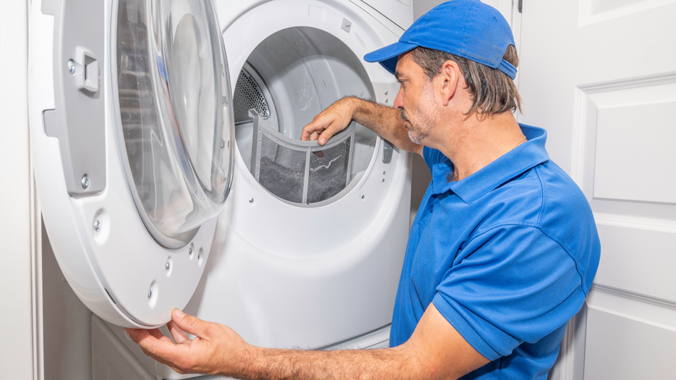 A white man in a blue polo shirt and ball cap lifts the lint screen out of a white dryer