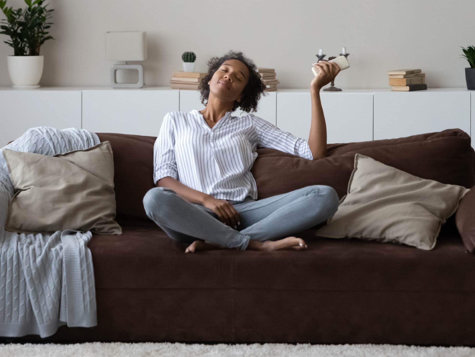 A Black woman sits nicely dressed, enjoying the air conditioning from the couch in her well-decorated living room