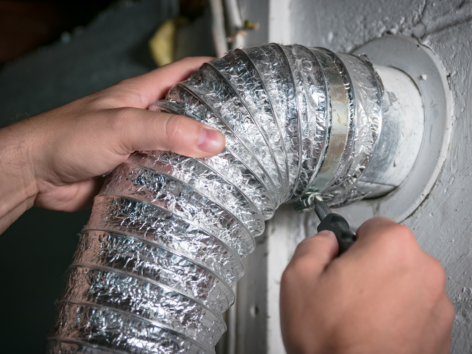 A person unscrews a screw holding an accordion foil pipe to a pipe coming out of the wall