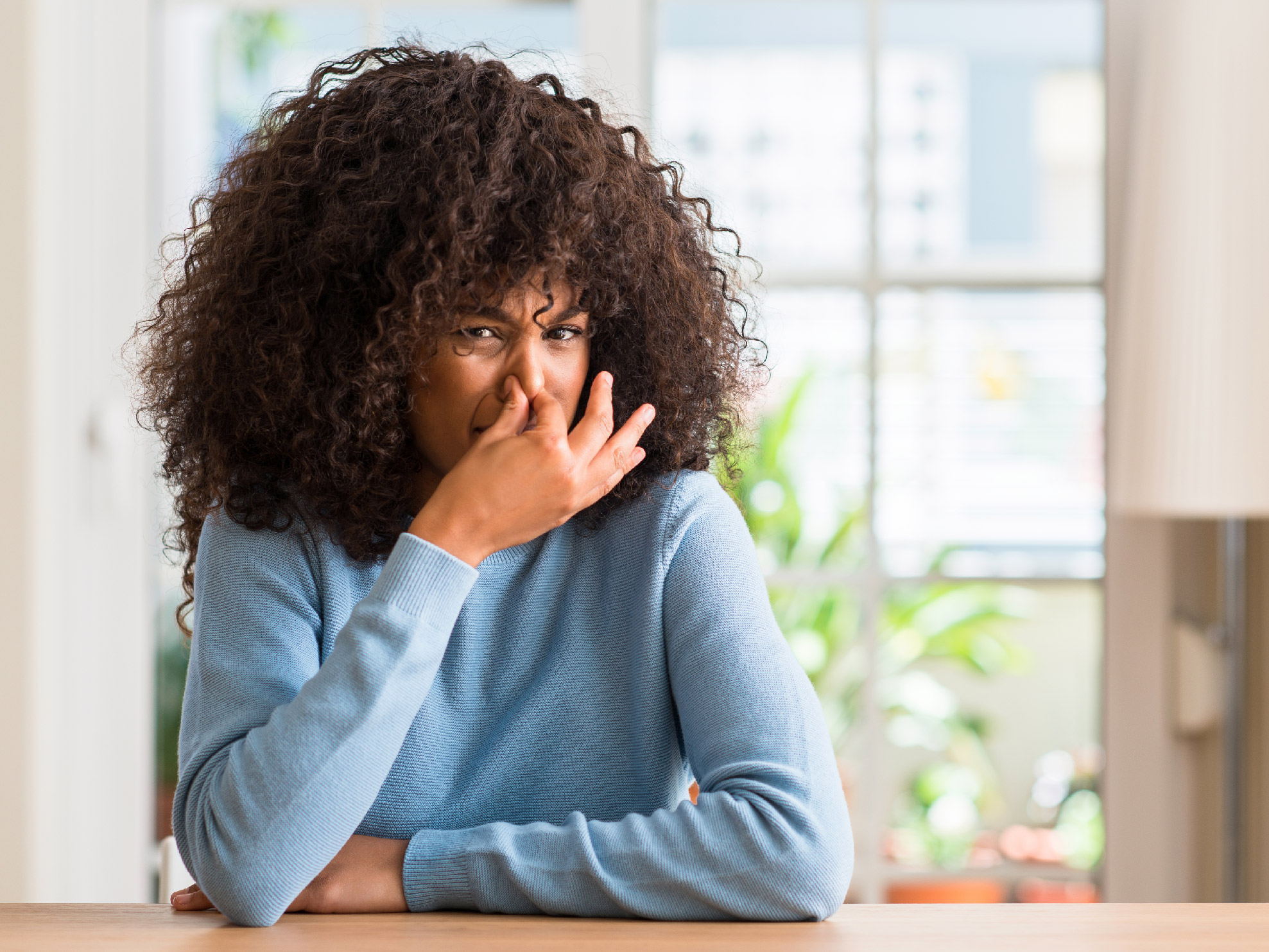 Woman pinches her nose while wearing a blue sweater