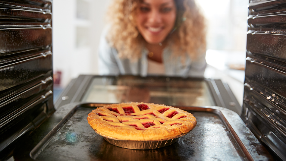 A woman smiles as she checks her pie in the oven