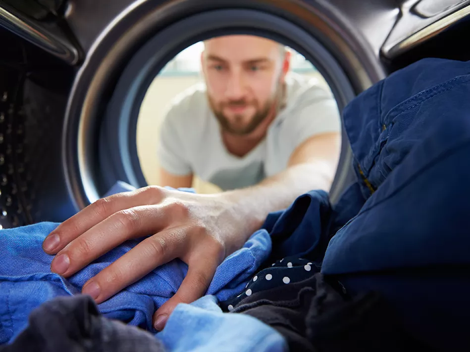 White man reaches left hand into the washer to grab one of many blue-colored items