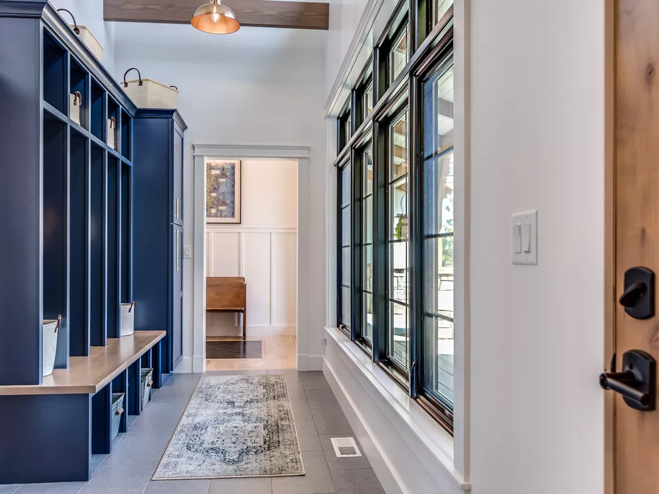 A grand navy and white mudroom features mudroom lockers and a pastel area rug in front of a wall of windows