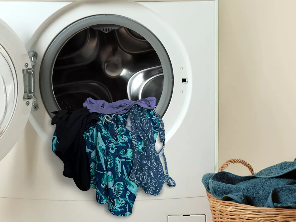 Swimsuits hang out of an open dryer next to a wicker laundry basket