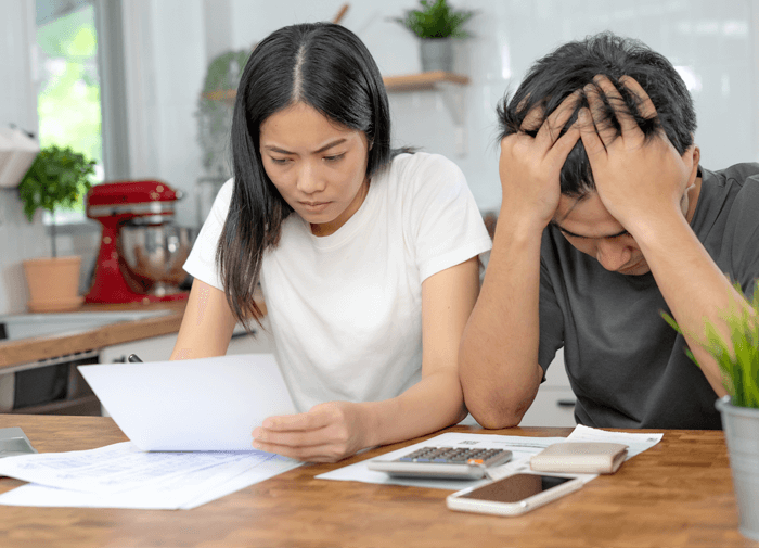 Worried couple reviewing financial documents at the kitchen table, using a calculator and notebook to manage bills or budget.