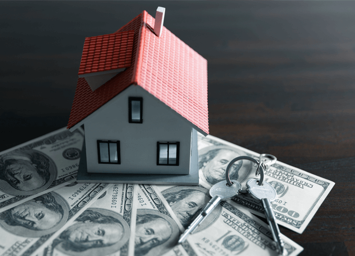 Miniature house model with keys on top of hundred-dollar bills, representing real estate investment, home purchase, or mortgage financing.